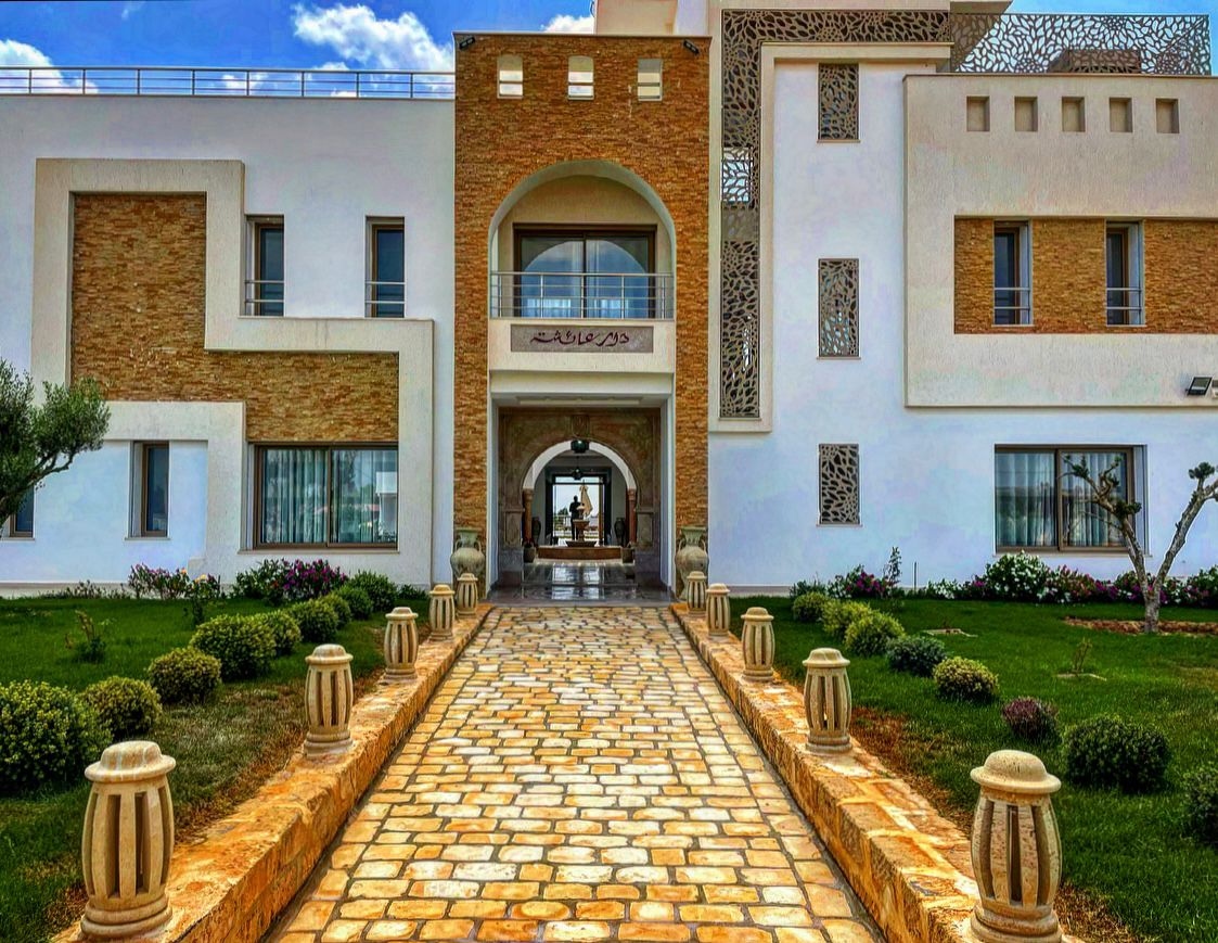 Allée d'entrée de la villa Dar Aïcha à Tazarka, architecture blanche contemporaine avec pierre locale, fronton gravé et jardin méditerranéen
