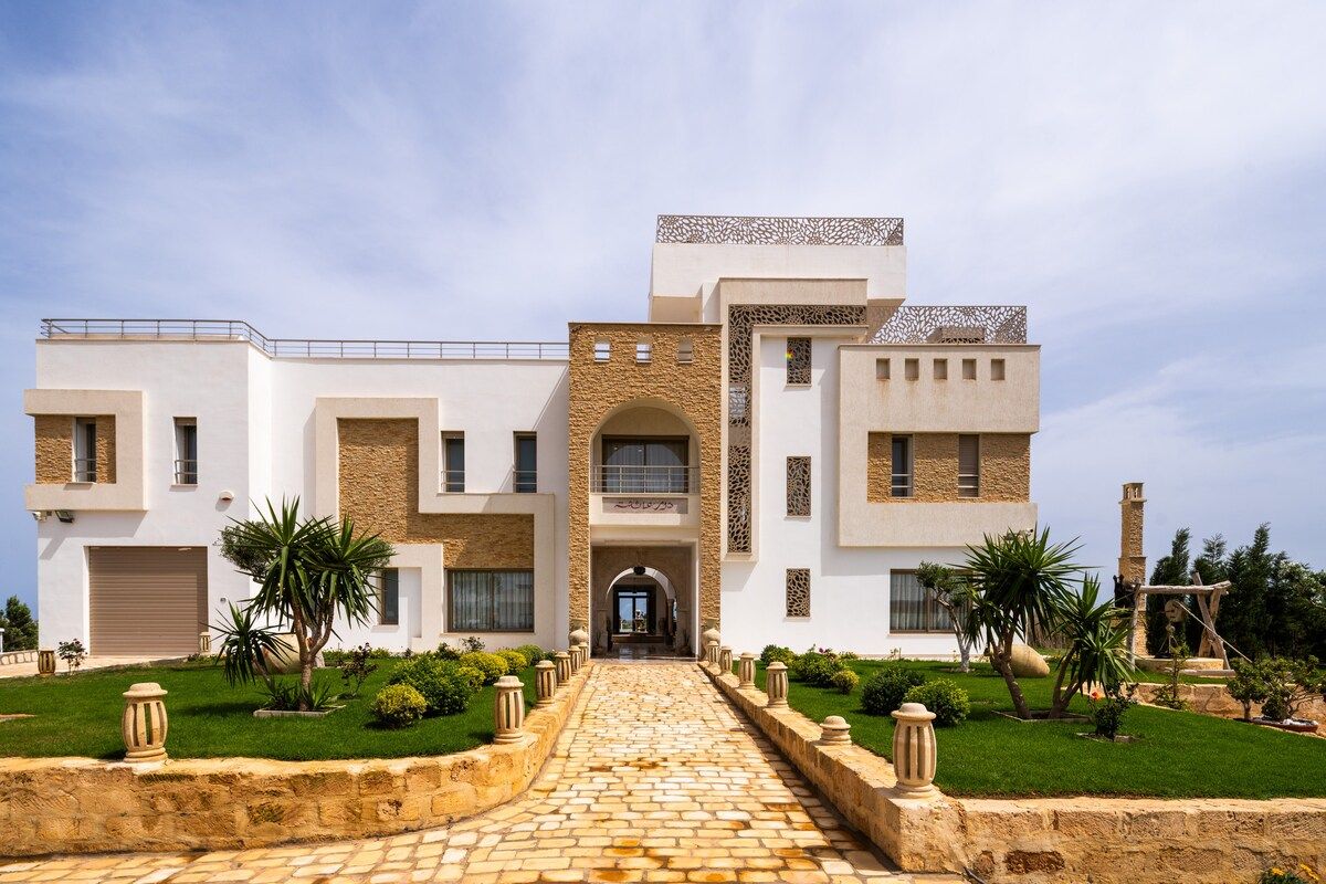 Vue frontale de la villa Dar Aïcha, façade blanche avec pierre dorée et allée pavée